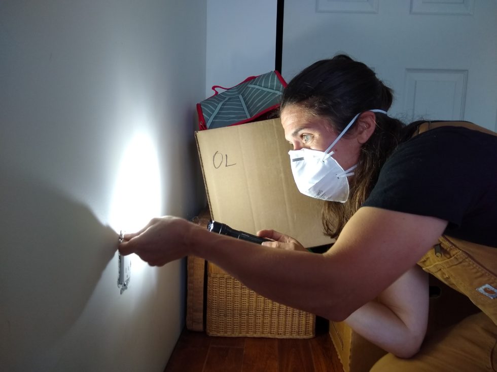Woman inspecting an electrical outlet with a flashlight.